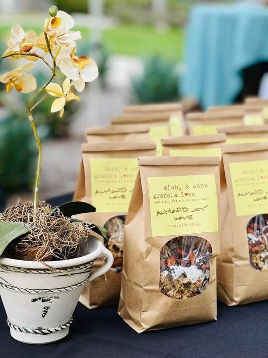 Kraft paper bags of Mishy & Sons Almond Joy Love granola on a table with an orchid